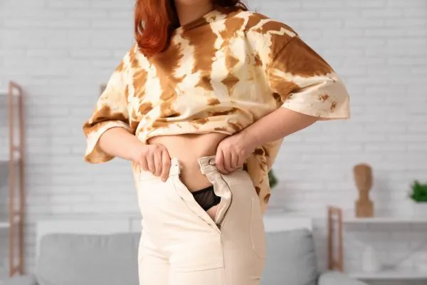 Image of woman trying to do her trousers up after pregnancy weight gain Springs Mire